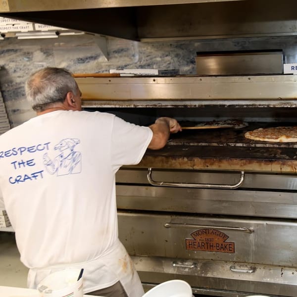 A pizza chef wearing a "Respect the Craft" shirt, baking pizzas in a Montague Hearth-Bake oven.
