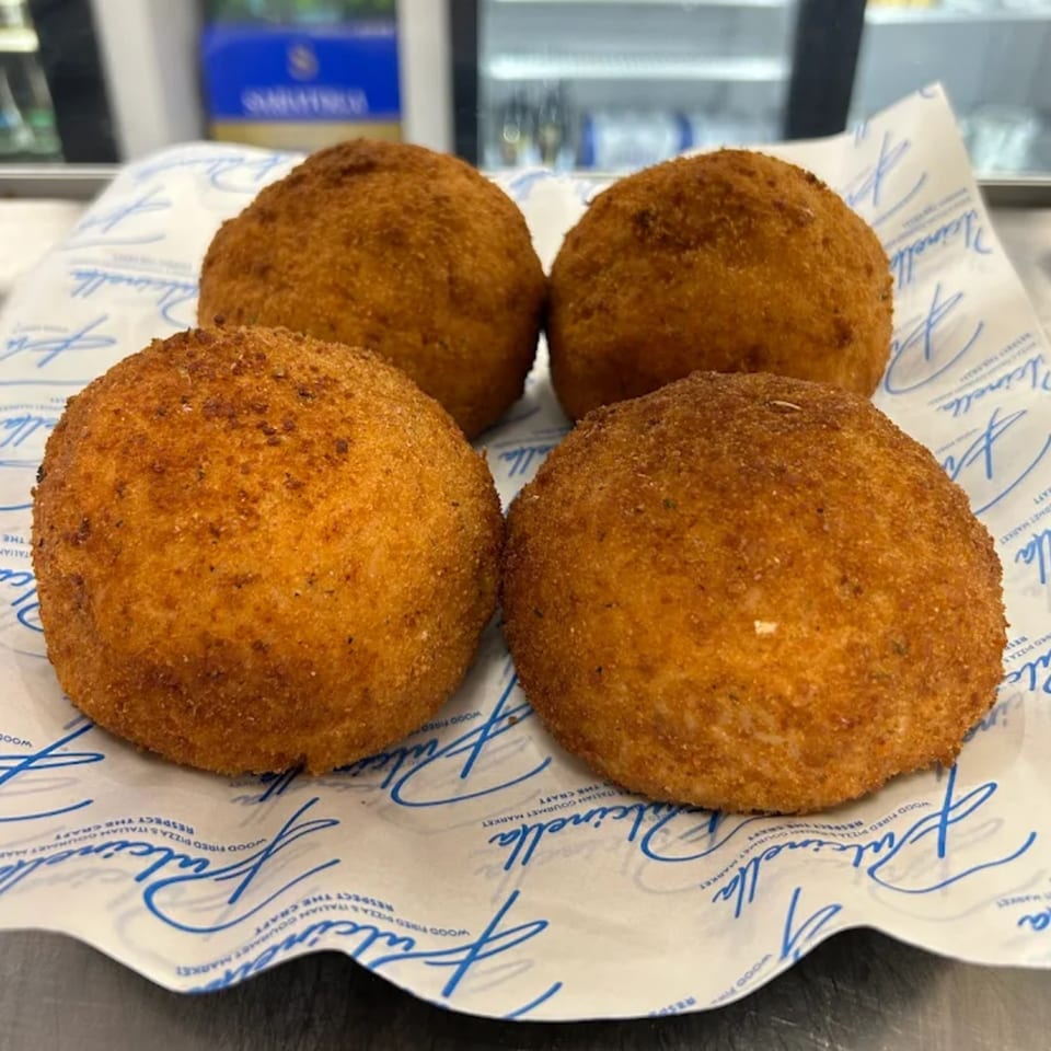 Four golden-brown arancini, Italian fried rice balls, resting on Pulcinella branded paper.