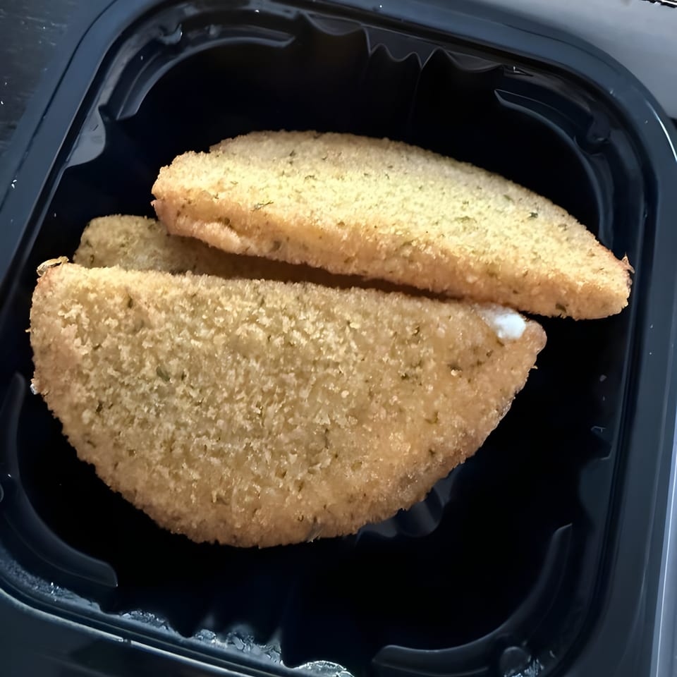 Two golden-brown, breaded Pulcinella calzones with a hint of white filling, in a black container.