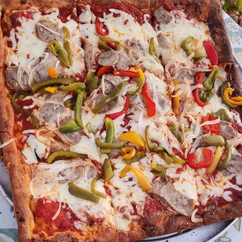 Close-up of a square Pulcinella pizza with sausage, onions, and colorful bell peppers.