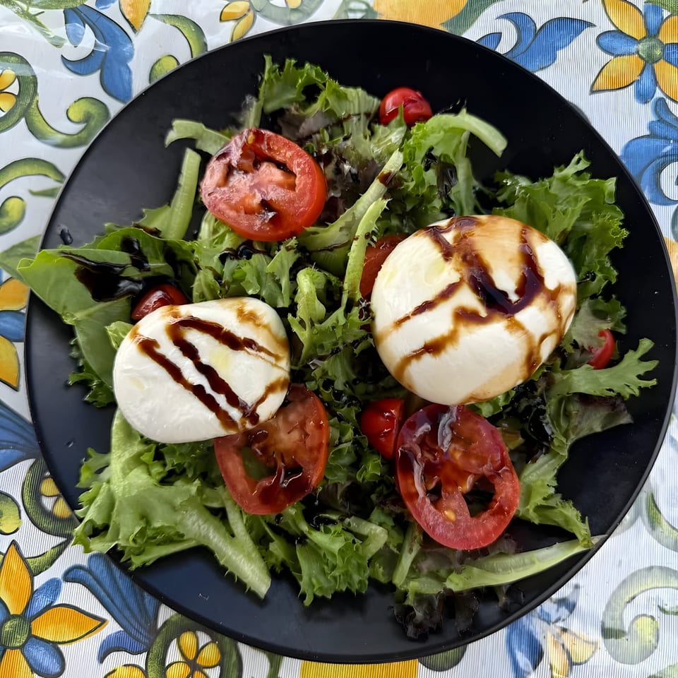 Caprese salad with fresh mozzarella, sliced tomatoes, and balsamic glaze on a bed of lettuce.