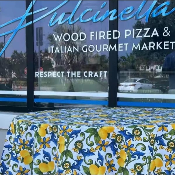Pulcinella Pizza and Italian Market storefront with a lemon-patterned tablecloth in the foreground.