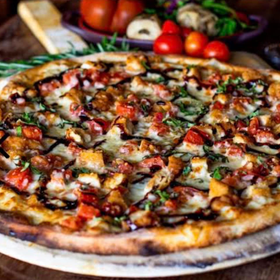 A delicious pizza with melted cheese, diced tomatoes, chicken, and a balsamic glaze drizzle.