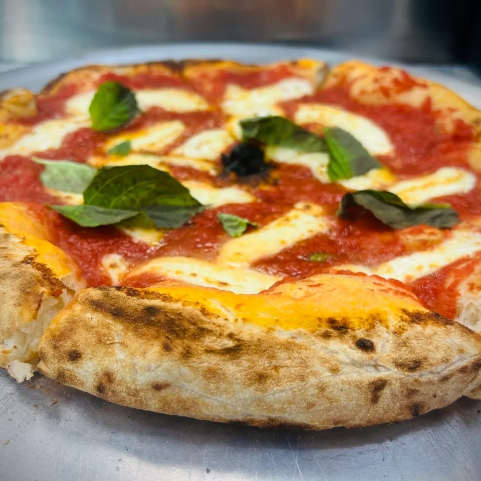 Close-up of a Pulcinella Margherita pizza with fresh basil, mozzarella, and tomato sauce.