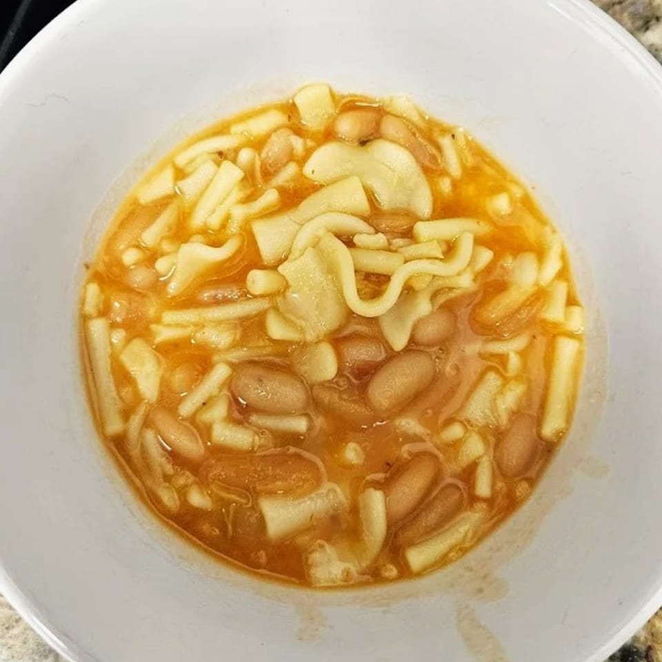 Close-up of a white bowl filled with pasta e fagioli, featuring beans and various pasta shapes.
