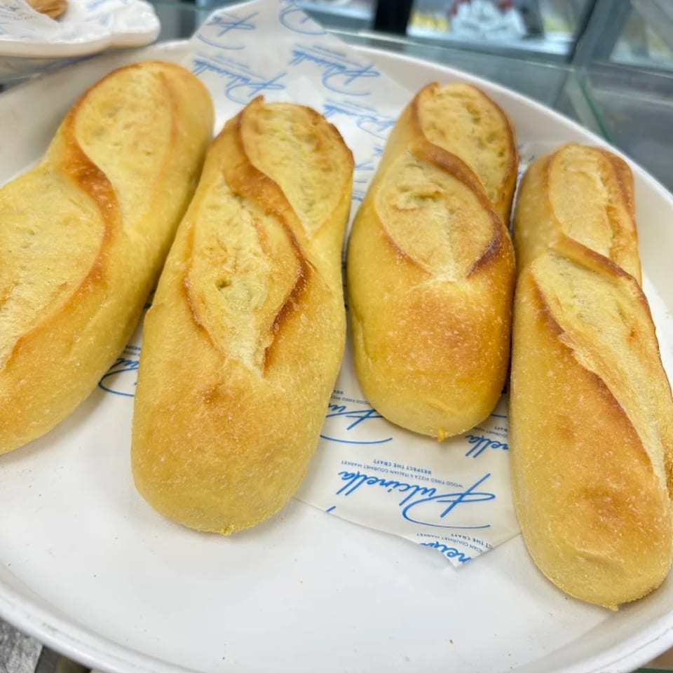 Four golden-brown mini baguettes, fresh from Pulcinella Pizza and Italian Market, on a white tray.
